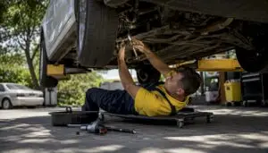 Mechanic inspecting ball joint under sedan